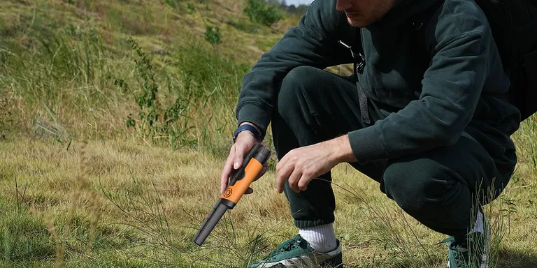 An orange SUNPOW pinpointer checks a plug cut in the grass